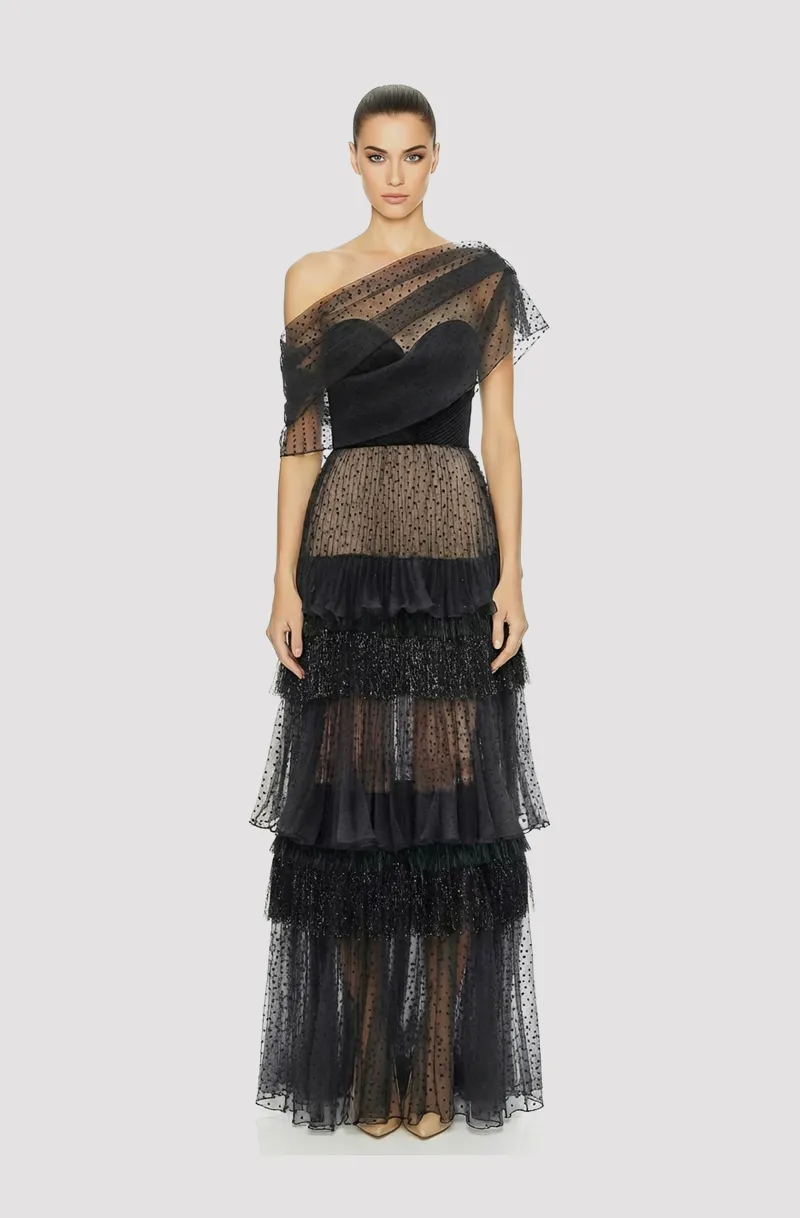 Front view of a woman in a Black strapless corseted gown with hand-draped bodice & dotted sheer organza tiered skirt accented w/ metallic fringe, with a detachable off-shoulder asymmetric overblouse 53, image 1